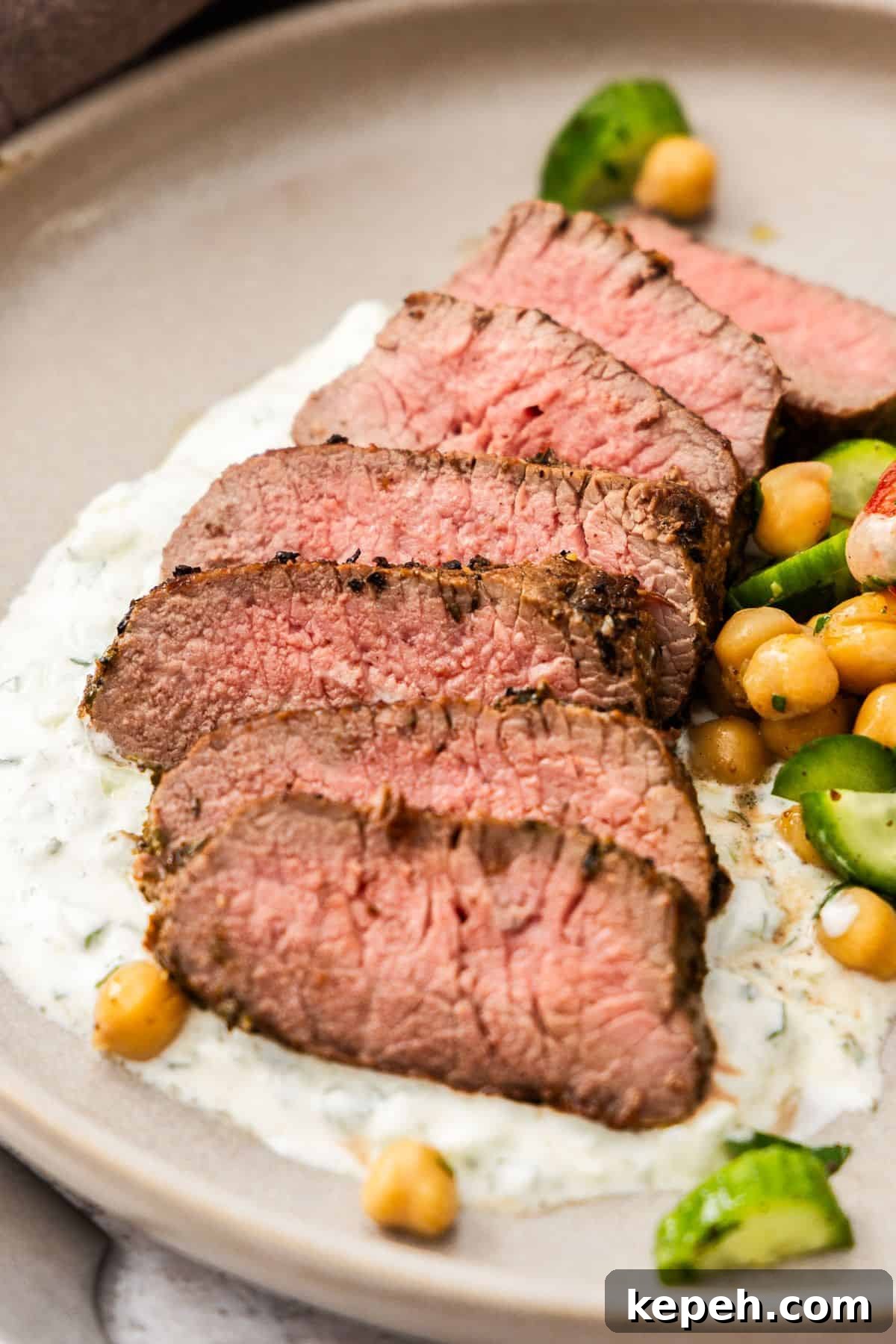 Top Easter Main Courses for a Memorable Holiday Meal 21 Round grey plate with a serving of sliced Lamb Backstrap, sitting on yoghurt sauce, with a chickpea cucumber side salad.