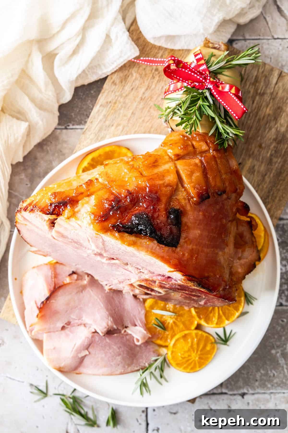 Top Easter Main Courses for a Memorable Holiday Meal 4 Marmalade Glazed Ham, sitting on a round white plate, with some slices of ham cut, and orange slices around the edge.
