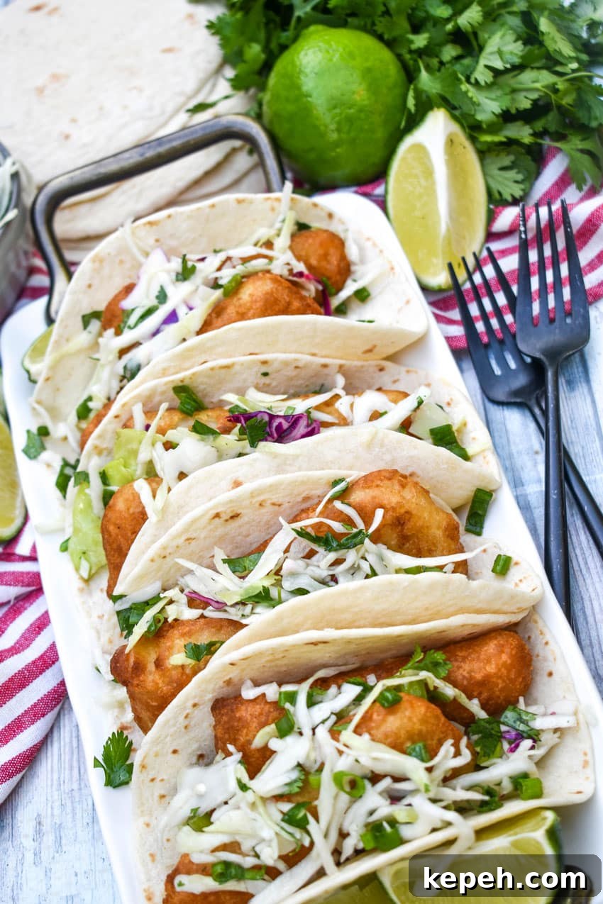 beer battered fish tacos arranged in a row on a white serving platter