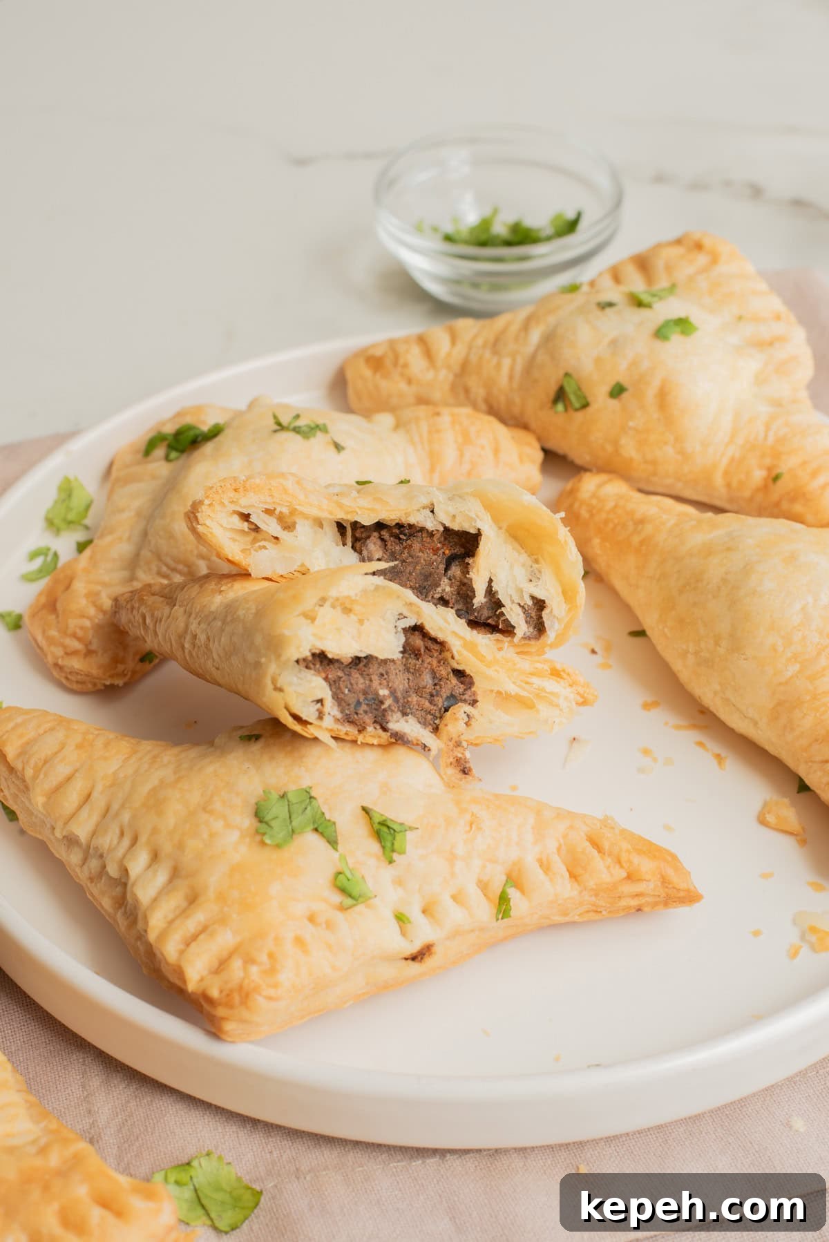 Authentic Jamaican Patty Recipe: Flaky Beef & Veggie Patties 2 A plate of patties with one cut in half to show the inside filling.