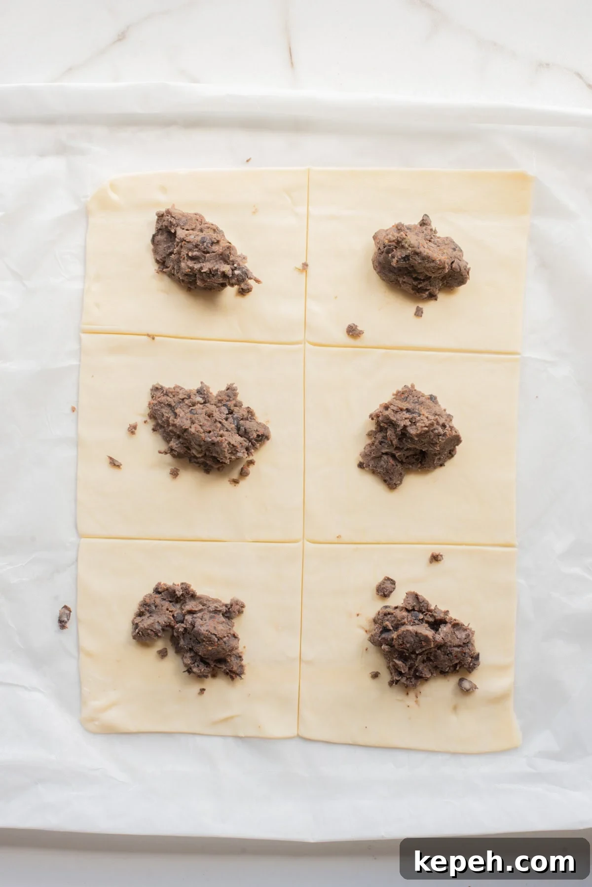 Authentic Jamaican Patty Recipe: Flaky Beef & Veggie Patties 7 Puff pastry sheets cut into rectangles with spoonfuls of bean mixture placed on top.