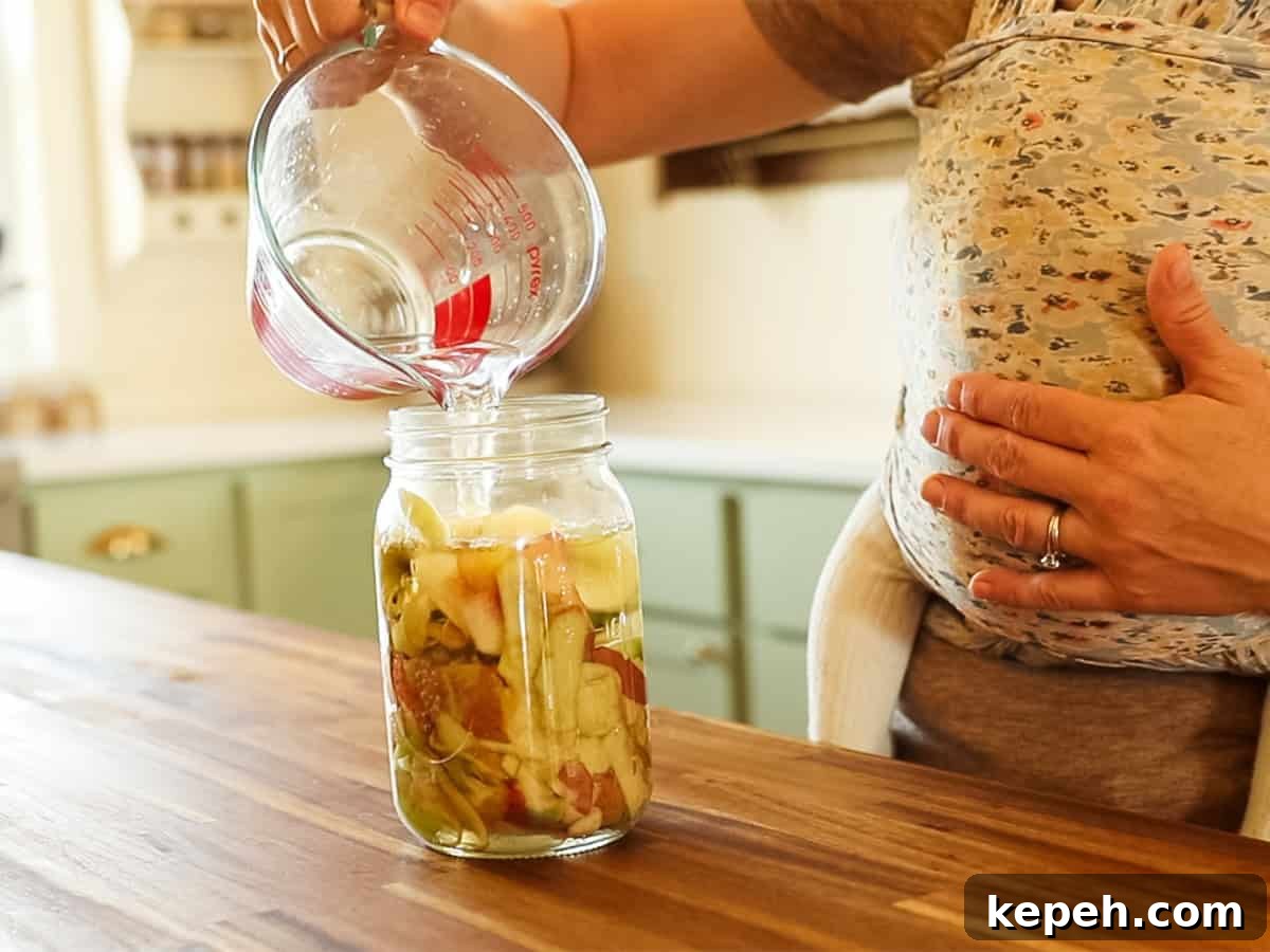 Homemade Apple Cider Vinegar Recipe for DIY Fermentation 5 Pouring water into a jar of apple cider scraps.