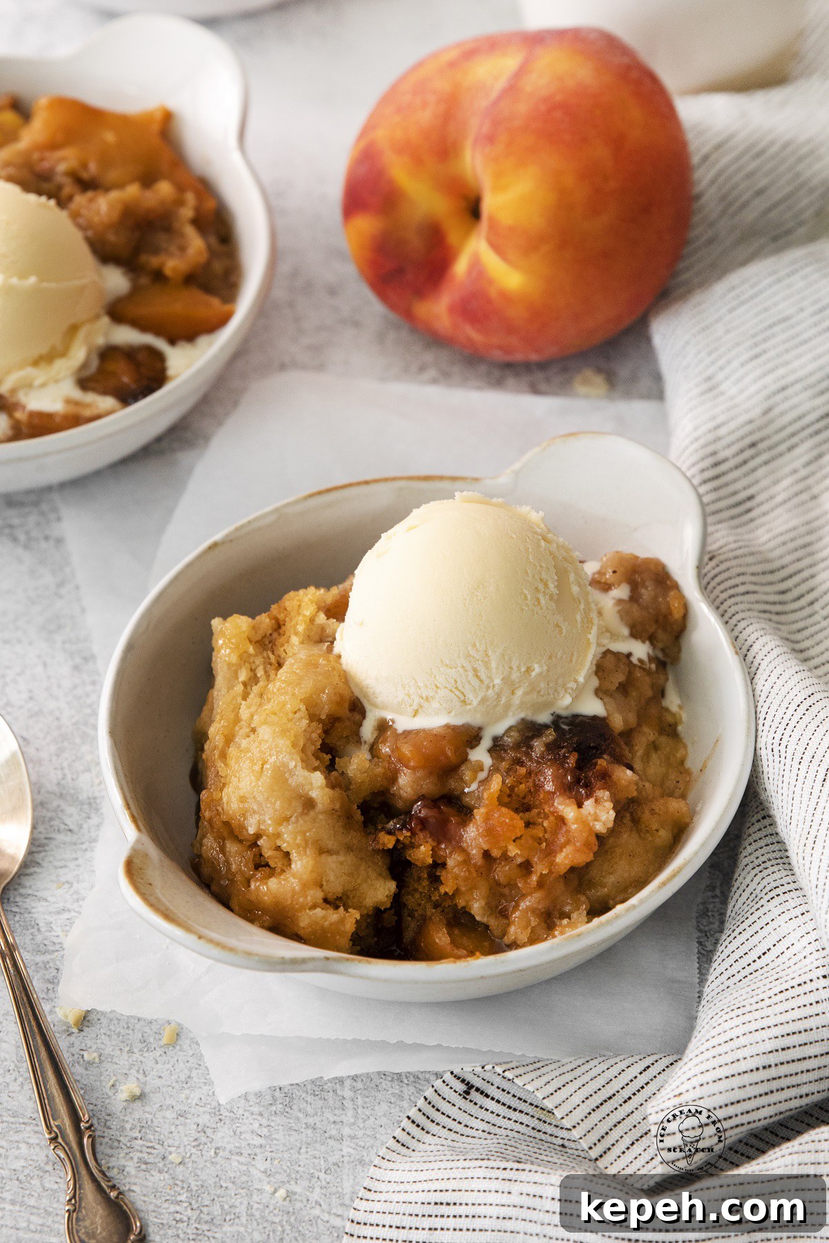 a ceramic bowl of easy peach cobber with a scoop of vanill ice cream melting into it.