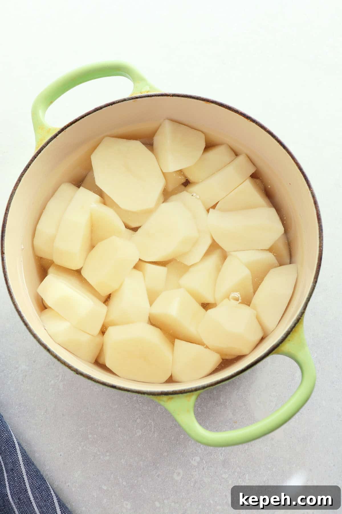 Classic Creamy Mashed Potatoes Recipe for Perfectly Smooth Results 5 Green small Dutch oven with raw potato chunks in water.