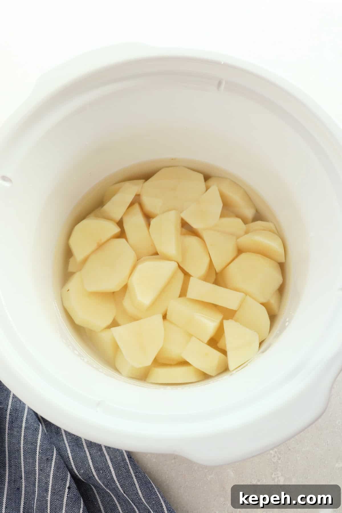 Classic Creamy Mashed Potatoes Recipe for Perfectly Smooth Results 6 Raw potatoes in water in white slow cooker.