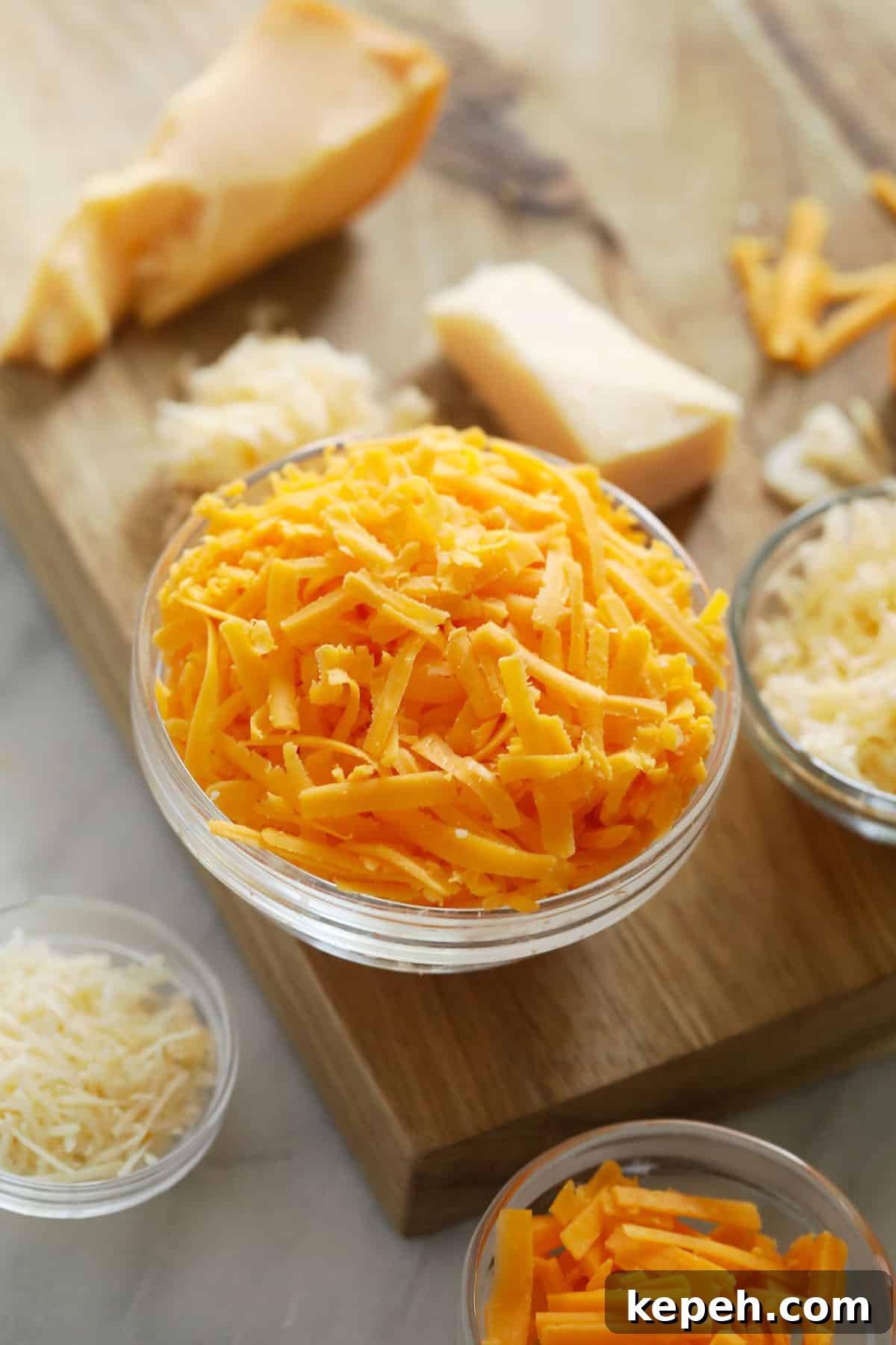 Many different grated cheeses on a cutting board.