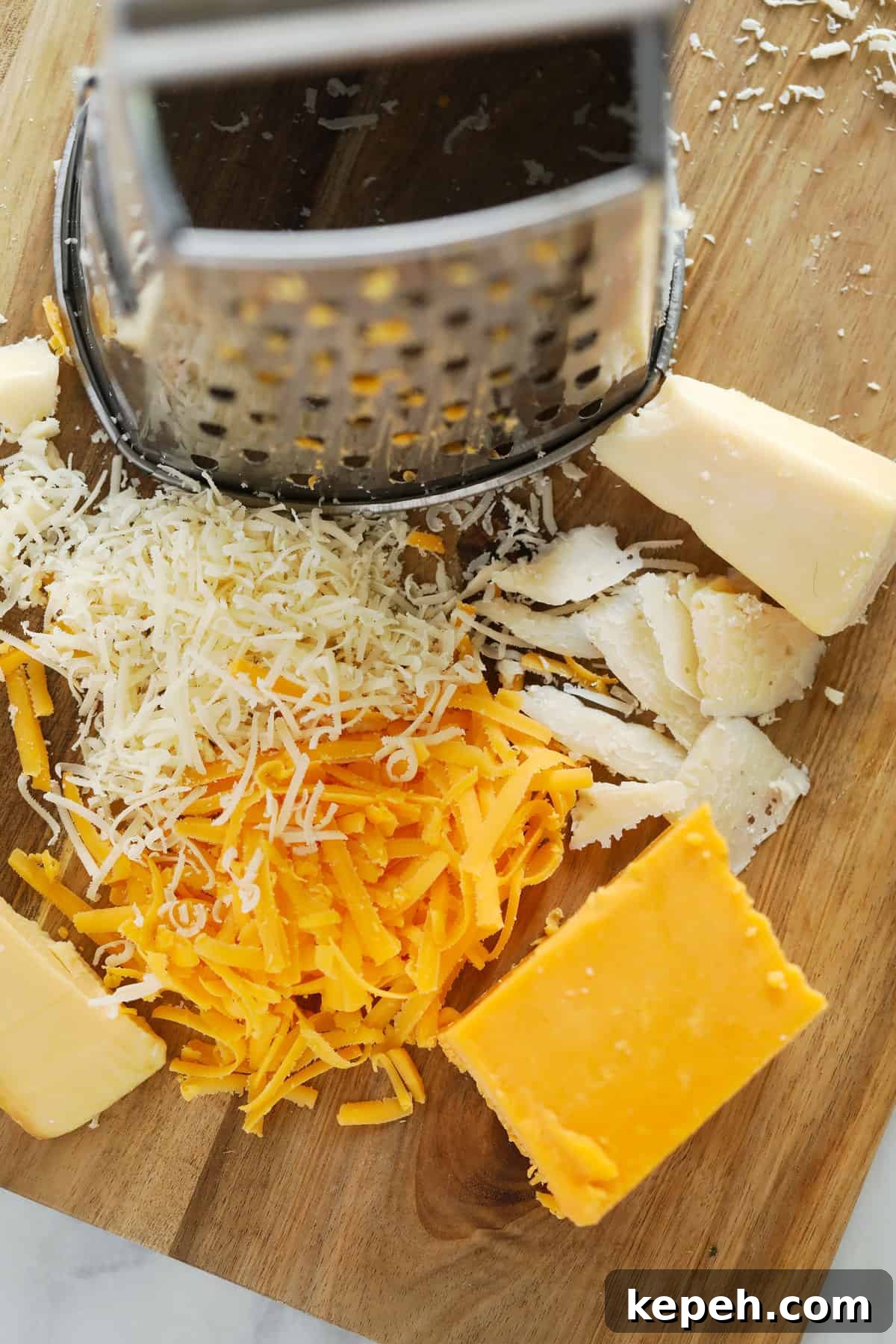 A box grater with different kinds of shredded cheese on the cutting board.