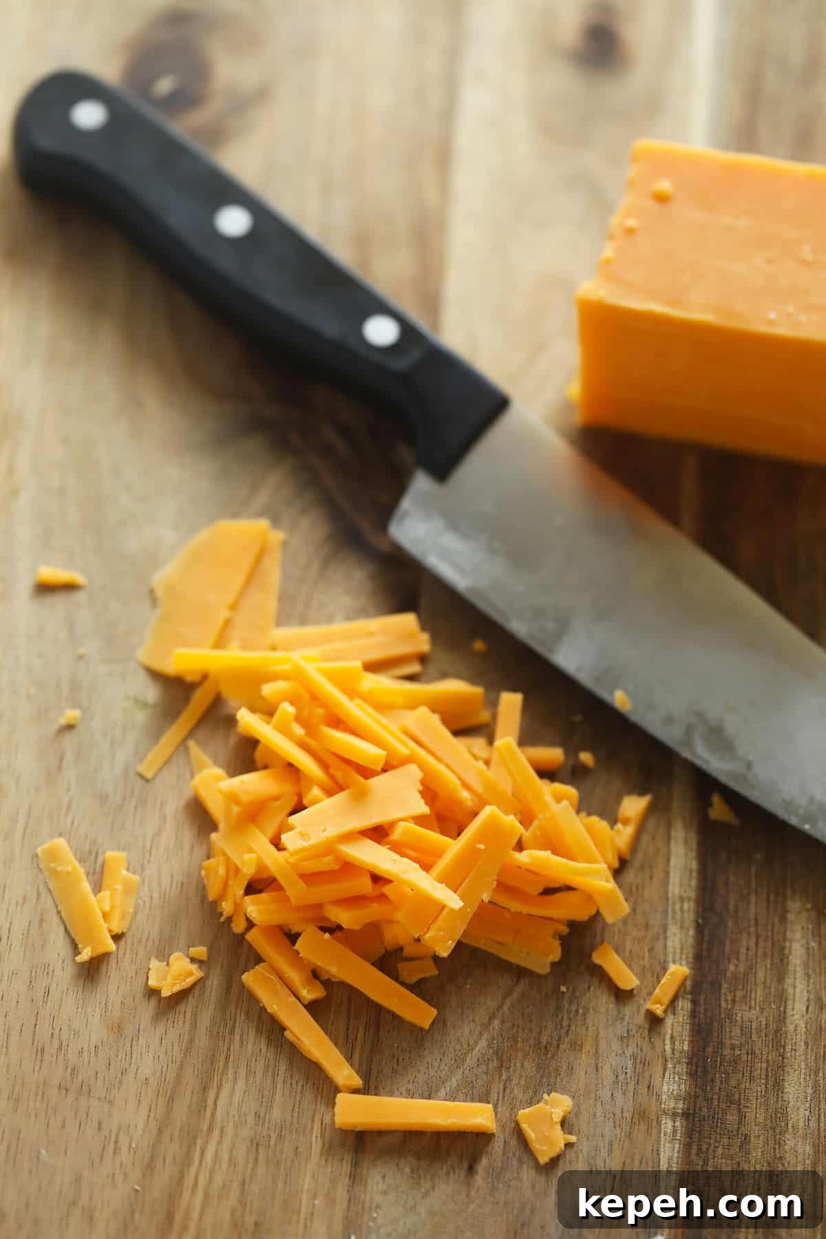 Shredded cheese on a cutting board by a knife.