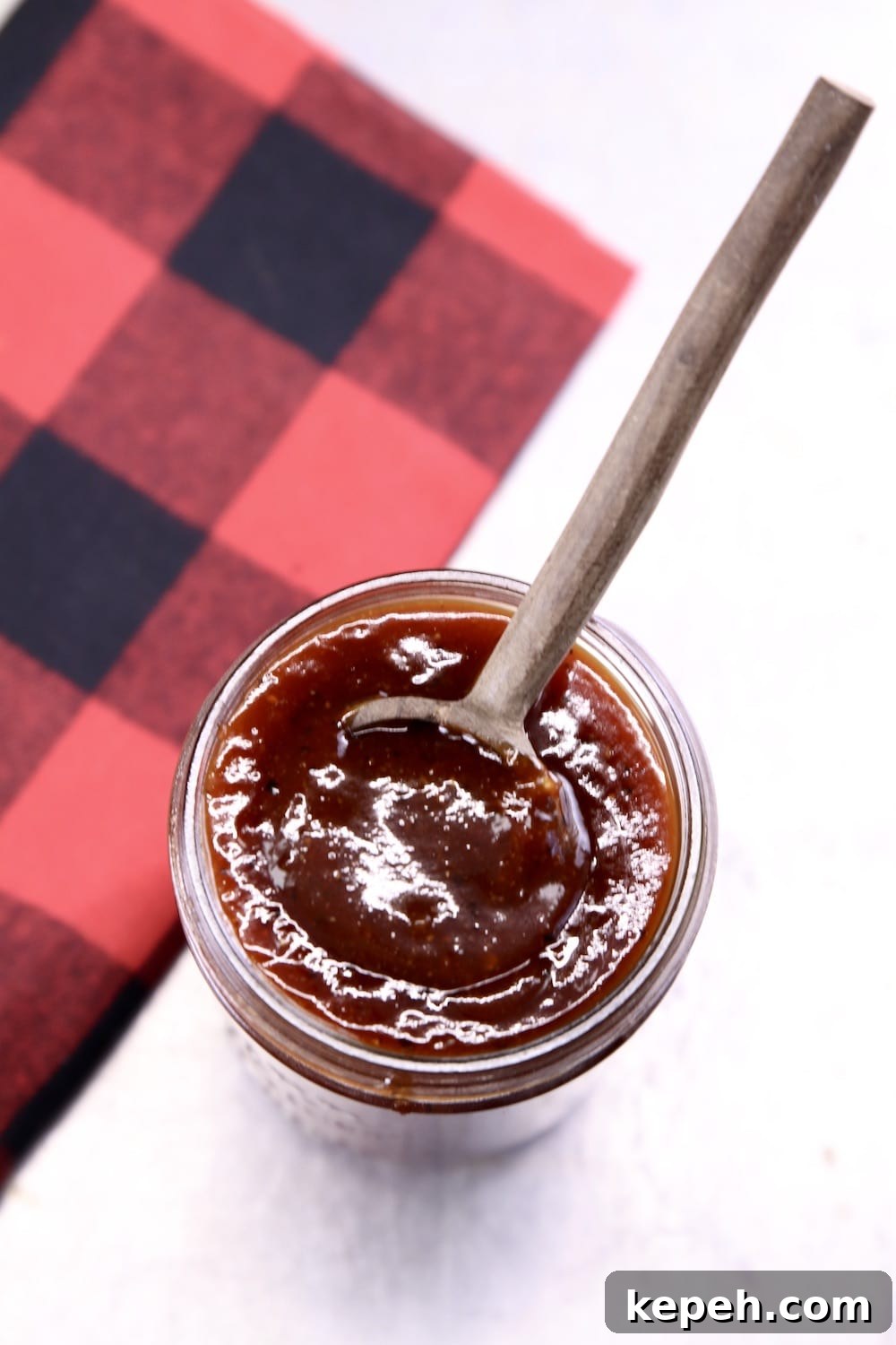 jar of bbq sauce with a wood spoon and buffalo check napkin