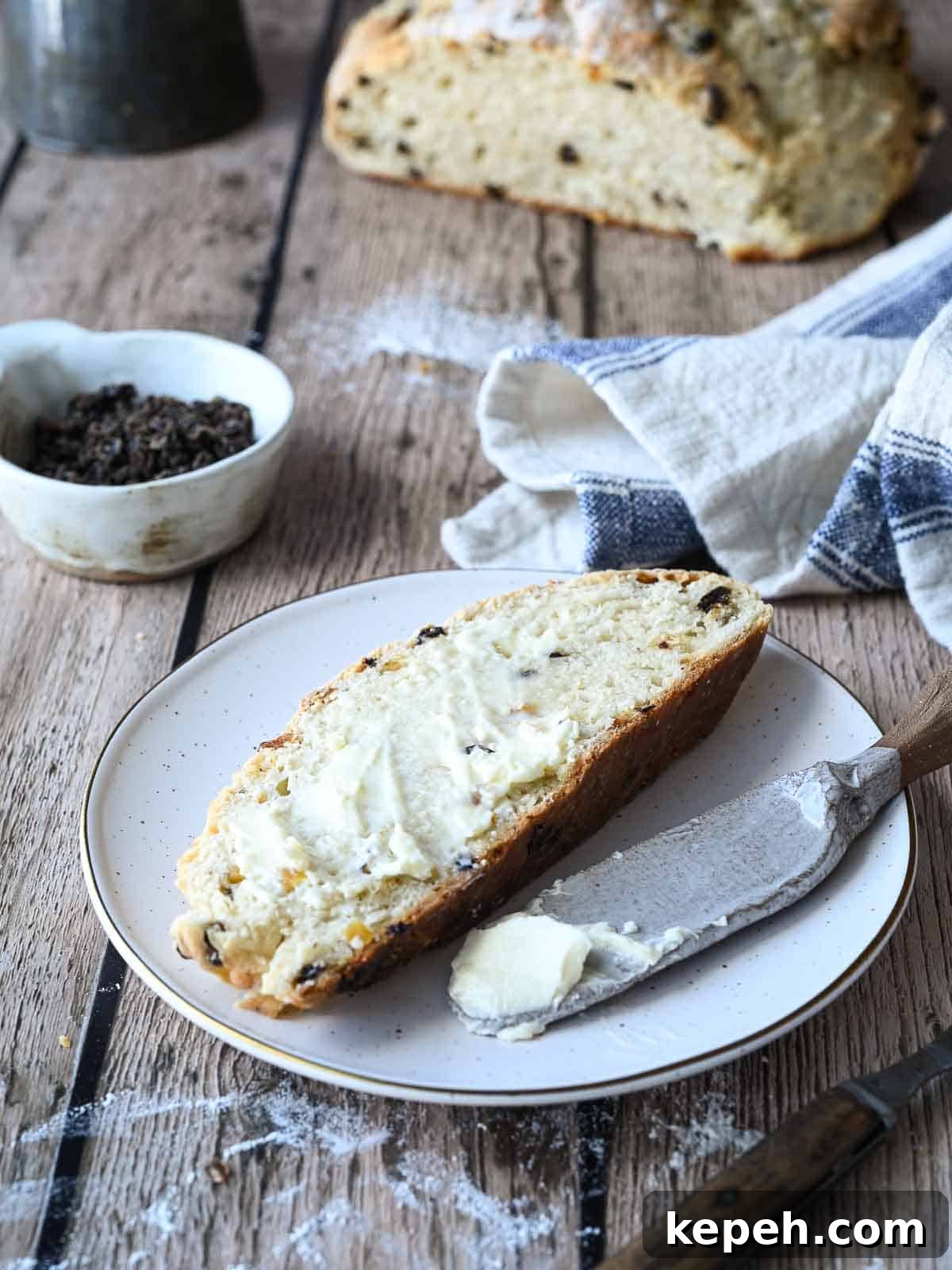 A slice of Irish soda bread with currants and apricots in the background.