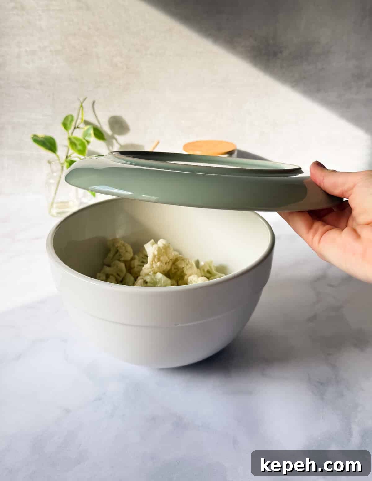 Garlic Butter Microwave Cauliflower Recipe for Quick Sides 5 covering a large bowl of cauliflower florets with a microwave-safe plate.