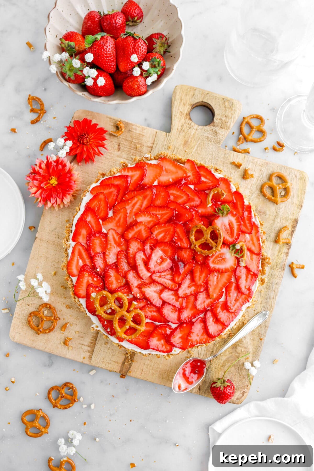 Strawberry Mascarpone Tart with Crunchy Pretzel Crust 2 strawberry tart on square wood serving board with pretzels, strawberries, and flowers around on marble surface and spoon of jam beside tart.