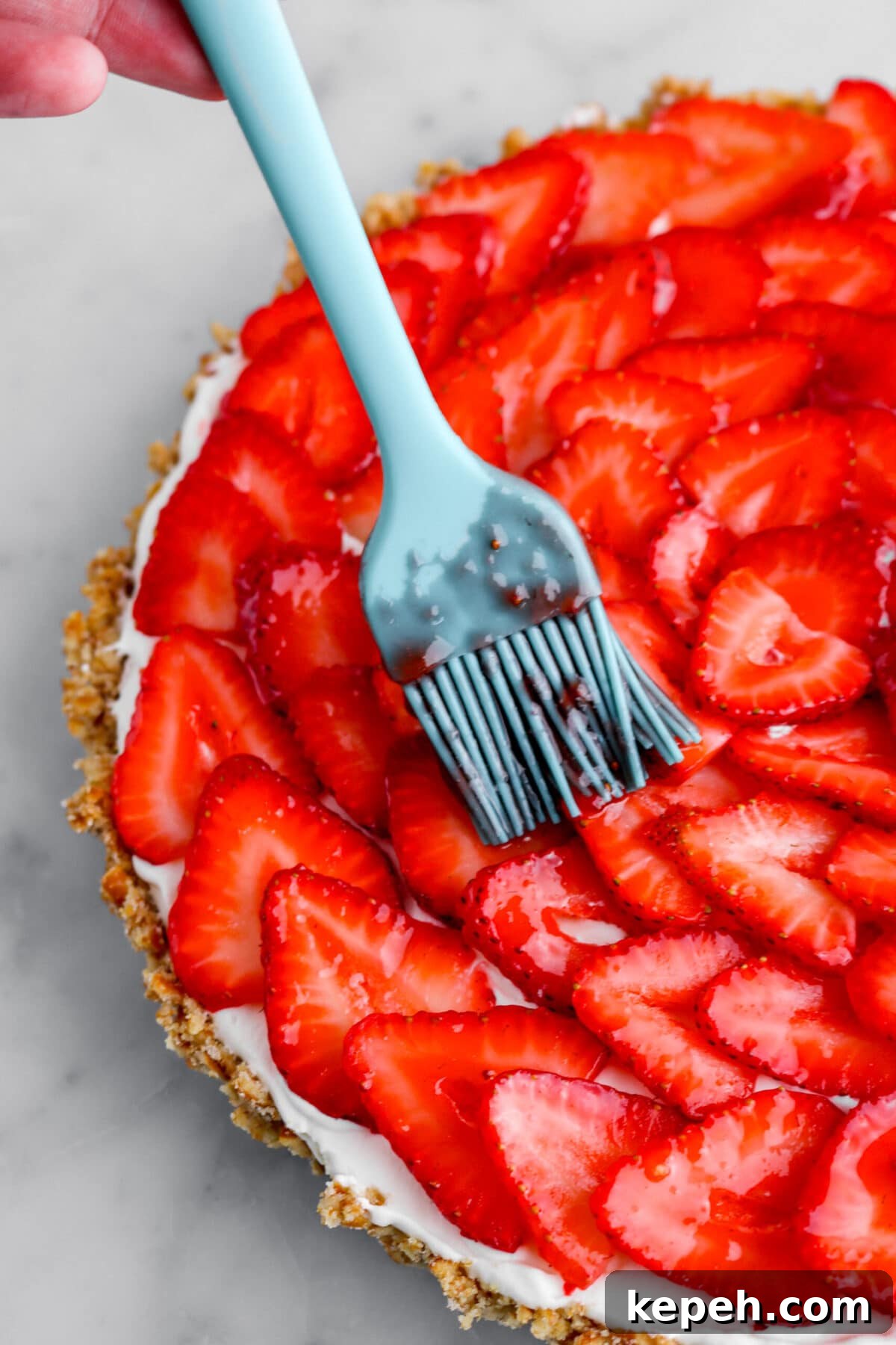 Strawberry Mascarpone Tart with Crunchy Pretzel Crust 18 jam being brushed on top of sliced strawberries.