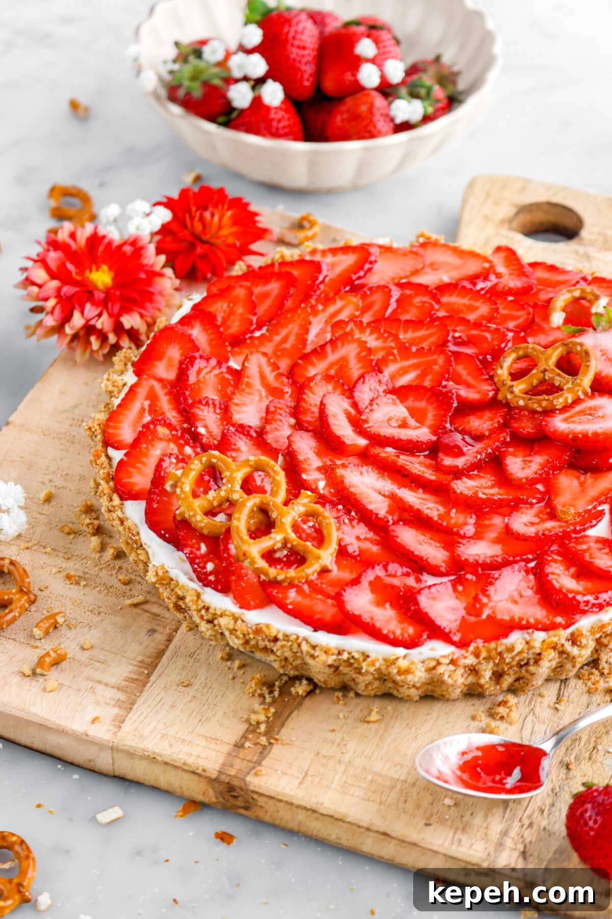 Strawberry Mascarpone Tart with Crunchy Pretzel Crust 19 cropped close up of strawberry tart on wood board with flowers around and bowl of strawberries behind.