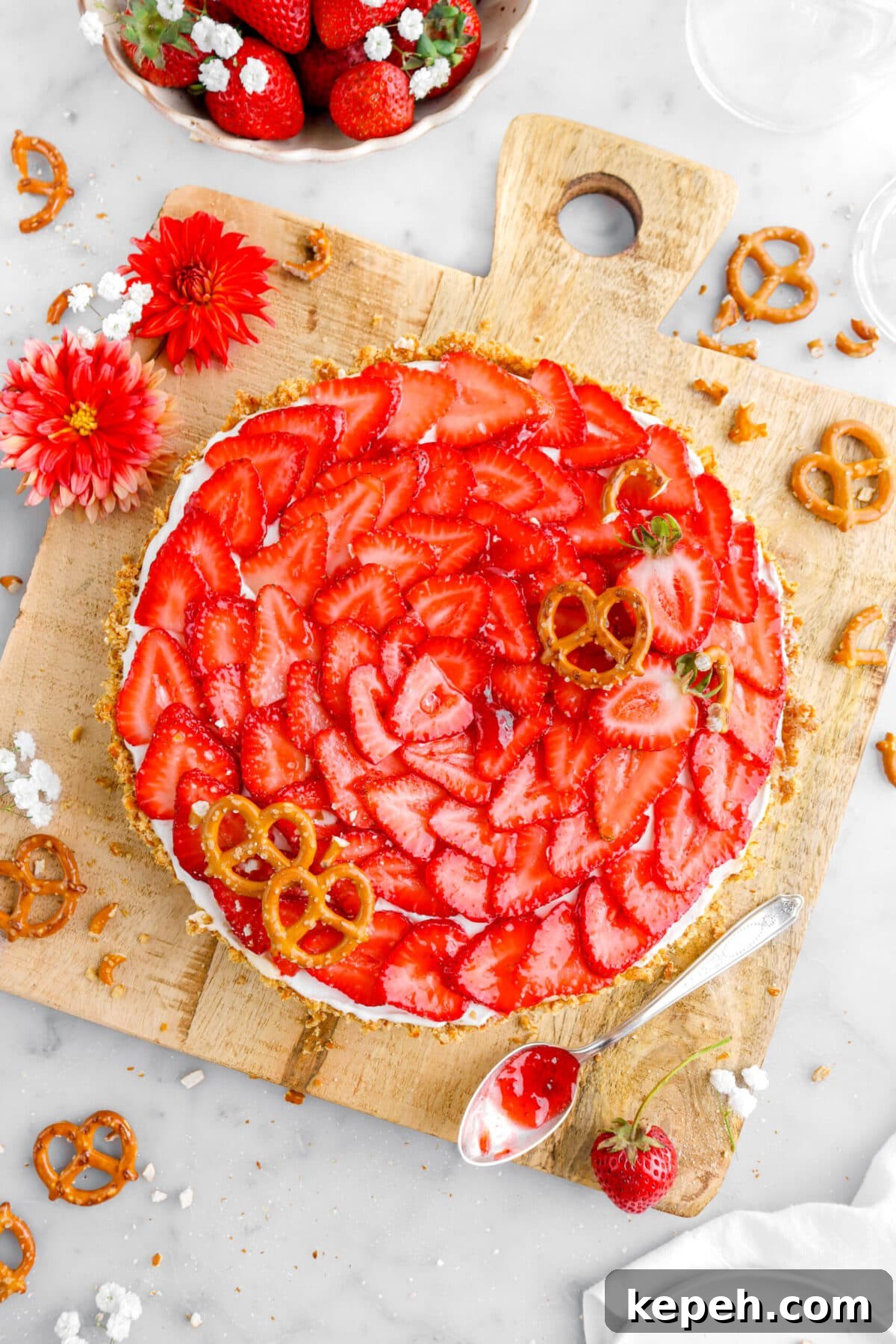 Strawberry Mascarpone Tart with Crunchy Pretzel Crust 5 overhead close up of strawberry tart with pretzels on top and more pretzels around on wood board with spoon of jam beside and flowers.
