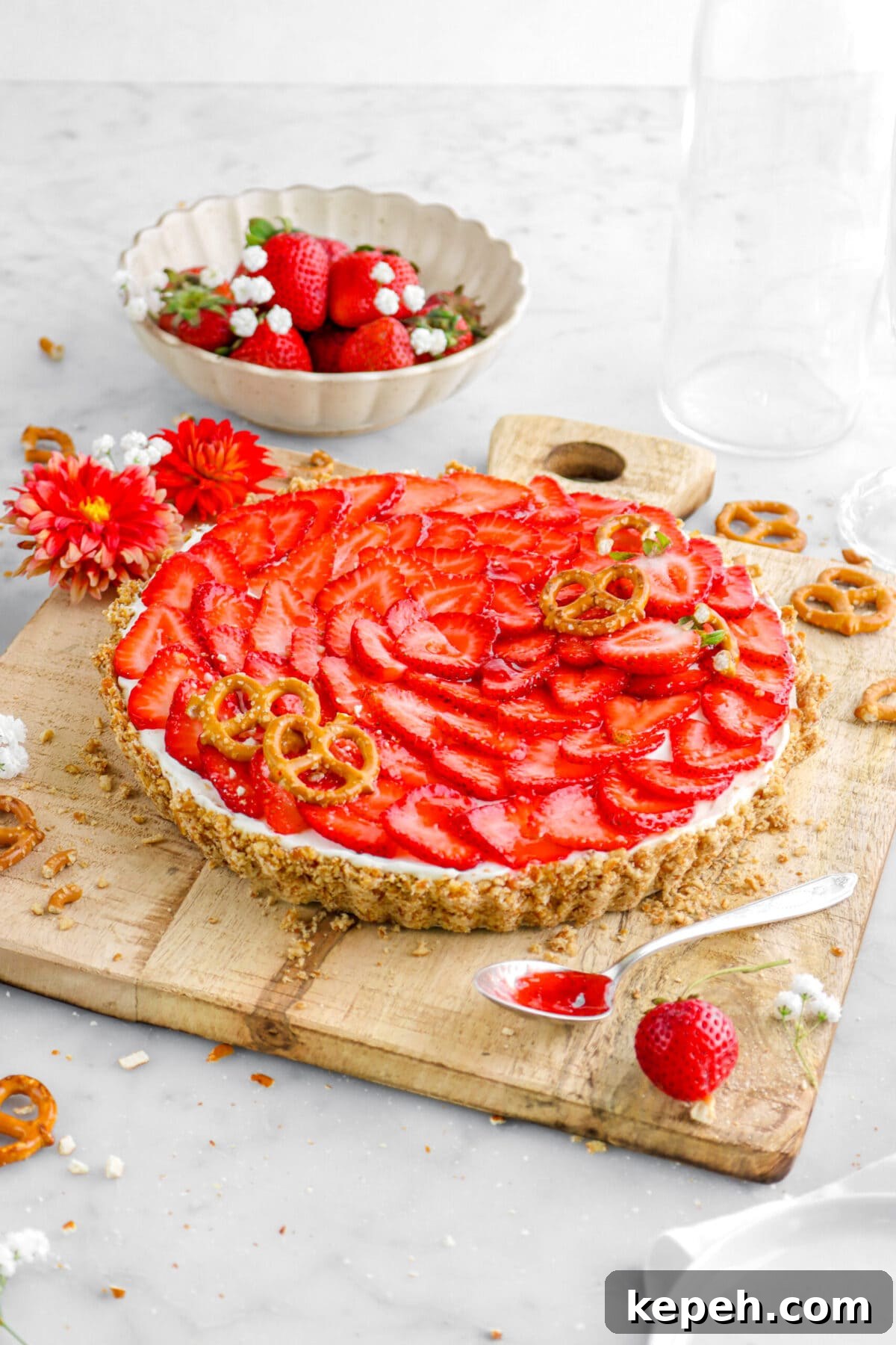 Strawberry Mascarpone Tart with Crunchy Pretzel Crust 6 angled shot of strawberry pretzel tart on square wood boards with flowers, strawberries, and pretzels around.