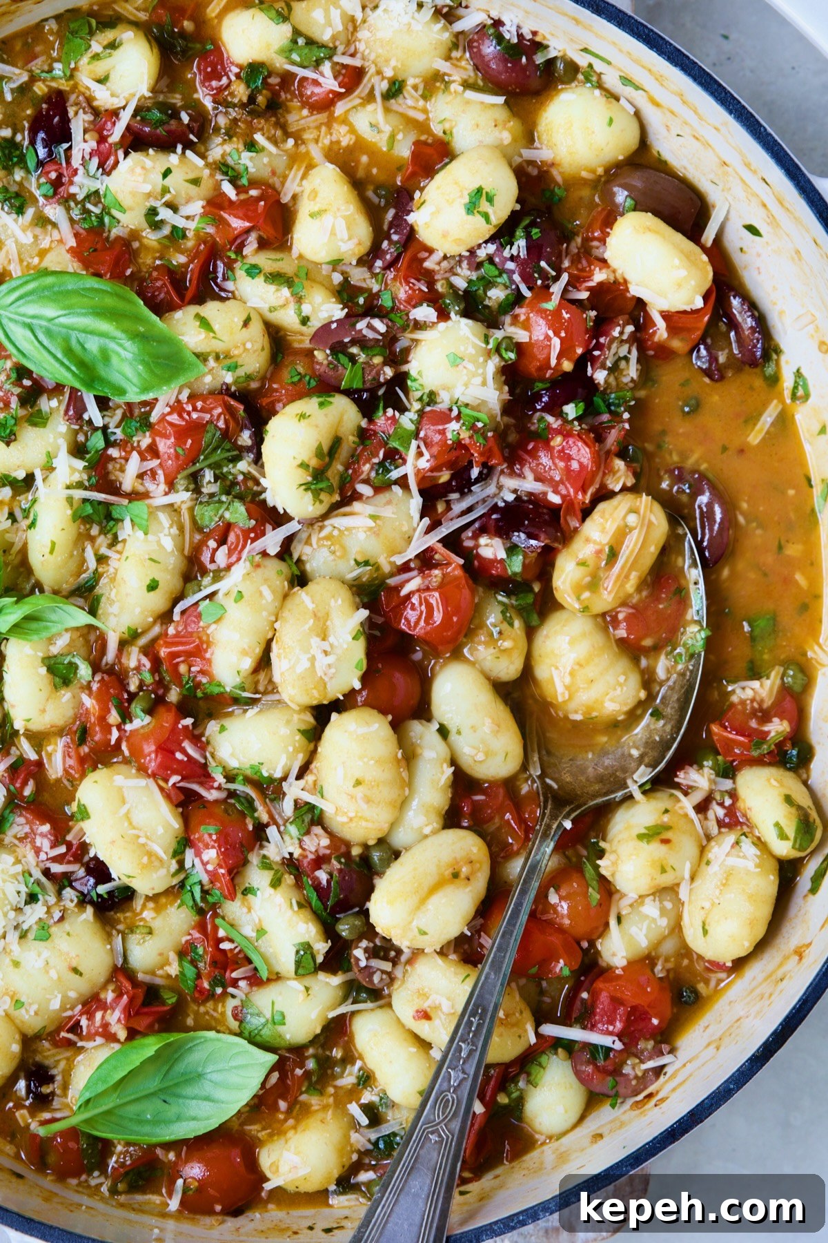 Gnocchi in Cherry Tomato Puttanesca Sauce 10 Gnocchi with Cherry Tomato Puttanesca Sauce with some on serving spoon in white enamel cast iron skillet.