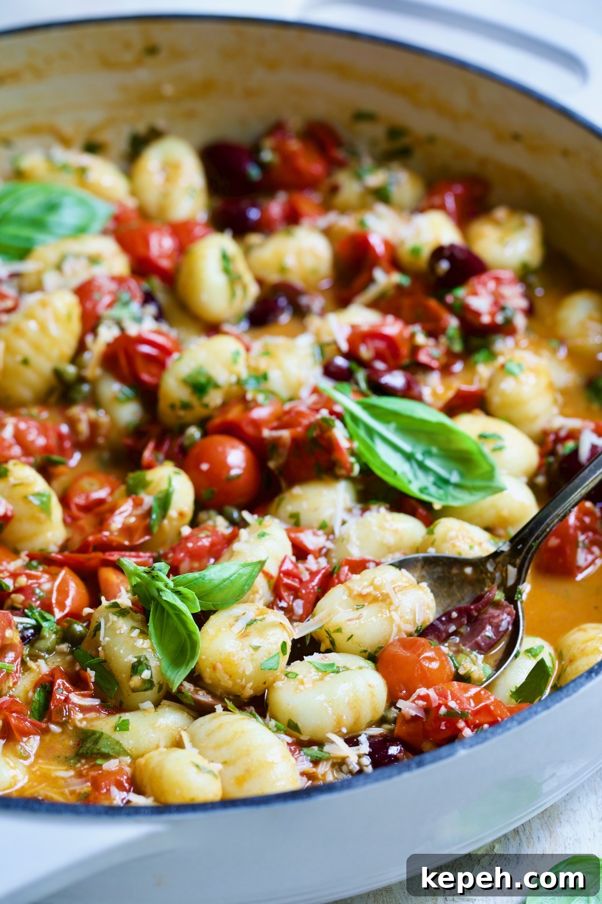 Gnocchi in Cherry Tomato Puttanesca Sauce 11 Gnocchi with Cherry Tomato Puttanesca Sauce in white enamel cast iron skillet with serving spoon scooping some up.
