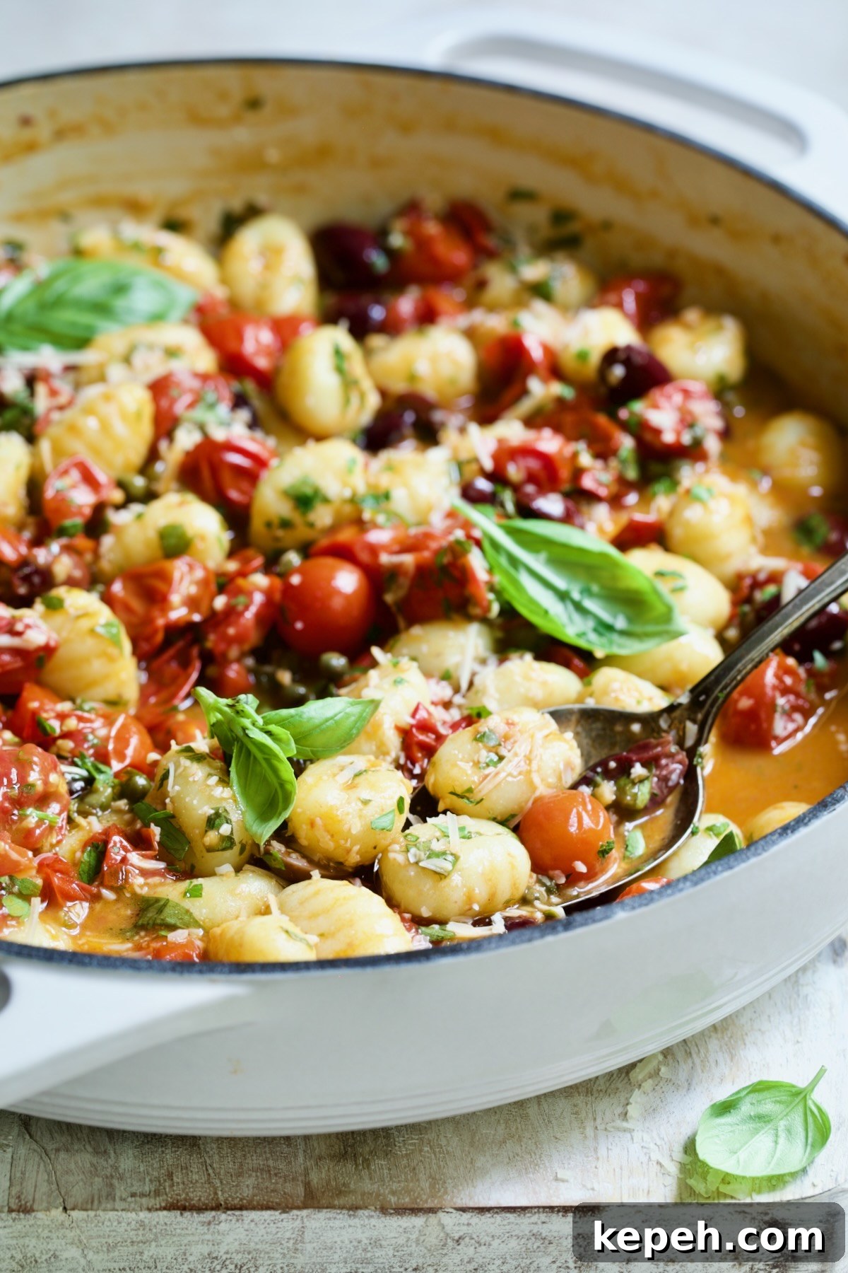 Gnocchi in Cherry Tomato Puttanesca Sauce 3 Gnocchi with Cherry Tomato Puttanesca Sauce in white enamel cast iron skillet with some on serving spoon.