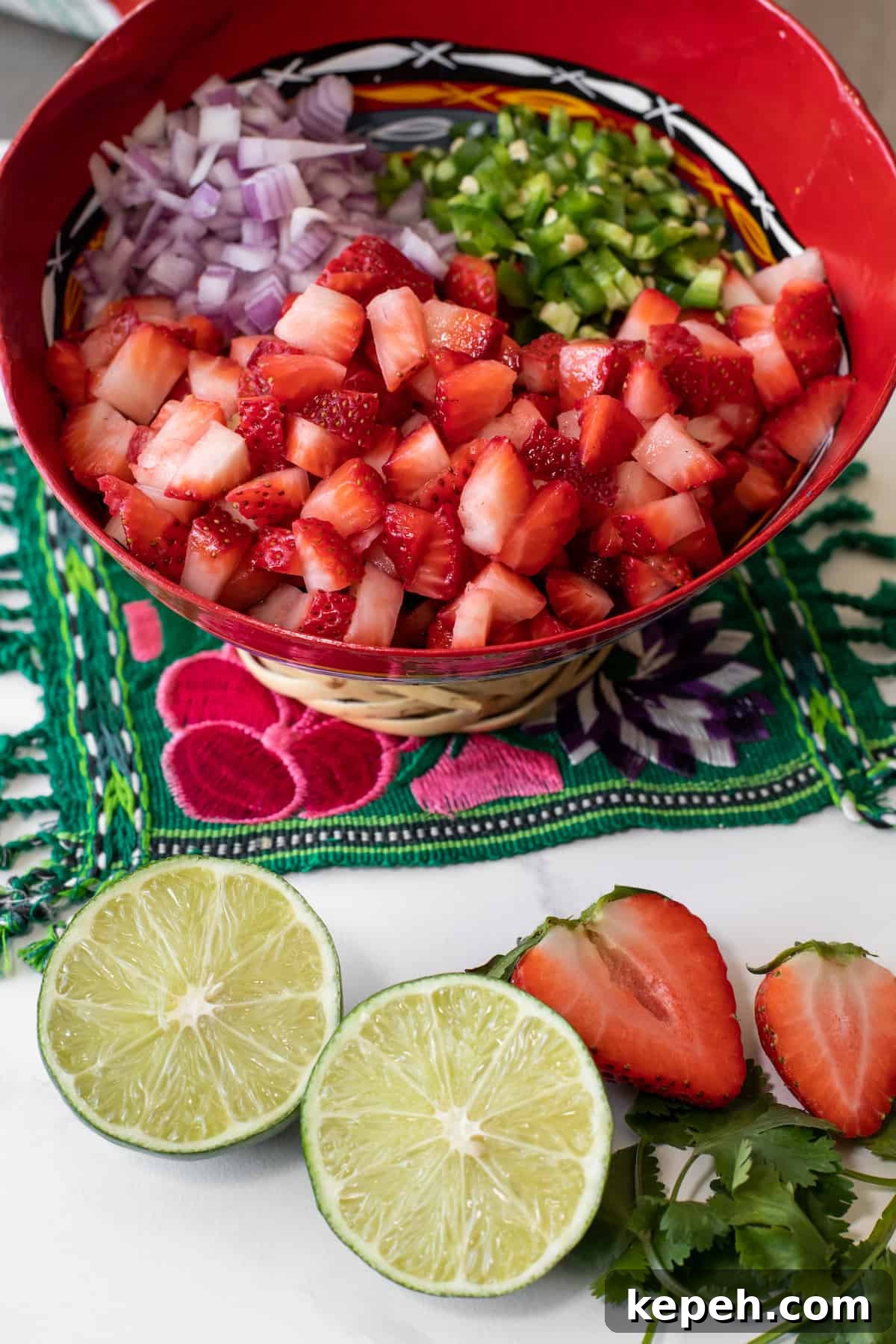 chopped strawberries, jalapeños, and red onions added to a red mixing-slash-serving bowl for making pico de gallo-style salsa. 