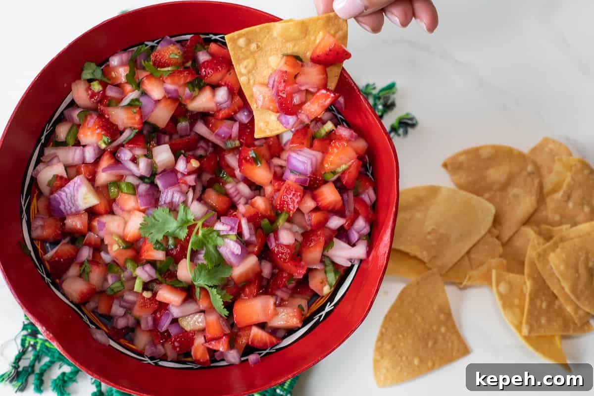 hand using a tortilla chip to scoop up spicy, savory strawberry pico de gallo salsa. 
