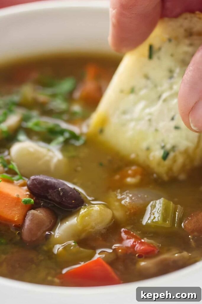 15-Bean Soup Recipe: Hearty, Protein-Packed Comfort Stew 5 Hand dipping garlic bread into vegetable and bean soup with visible veggies.