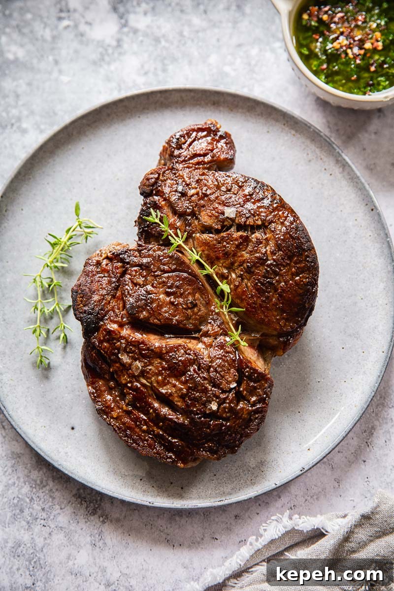 cooked ribeye steak on grey plate and a small dish of herb sauce near it