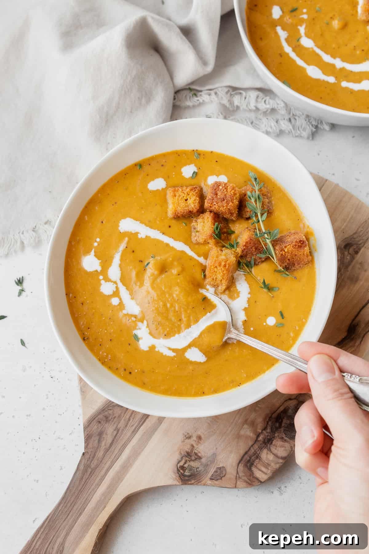 Creamy Plant-Based Pumpkin Soup Recipe for Fall Comfort 11 Hand taking a spoonful of vegan pumpkin bisque from the garnished bowl of soup.