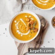 Creamy Plant-Based Pumpkin Soup Recipe for Fall Comfort 12 Overhead shot of a bowl of vegan pumpkin bisque garnished with thyme, croutons, and a drizzle of vegan cream.