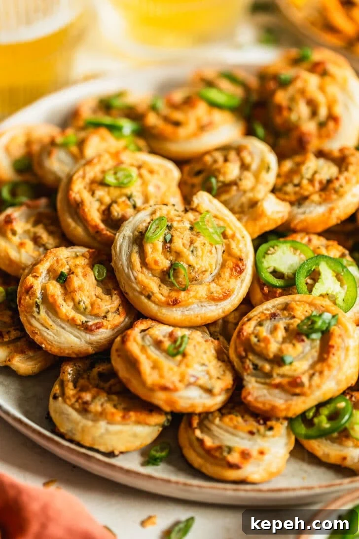 A beige plate of baked jalapeño popper pinwheels on a tan counter next to glasses of beer and an orange linen.