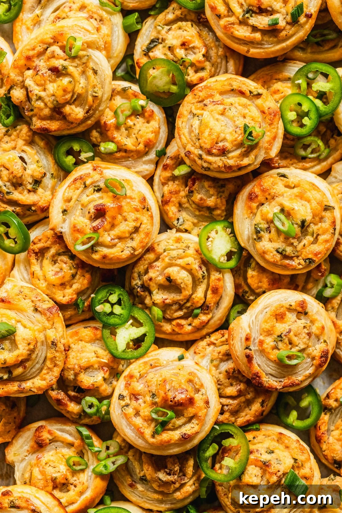 Rows and stacks of puff pastry jalapeño popper pinwheels garnished with sliced jalapeños and green onions.