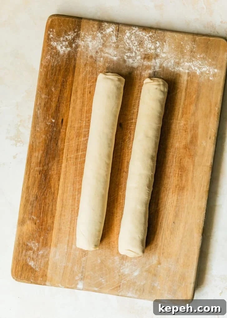 Two puff pastry logs of jalapeño popper pinwheels on a wood board.