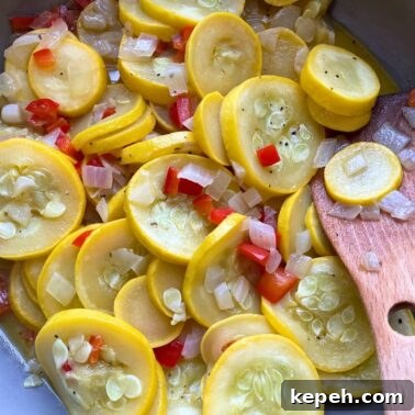 A blue and gray frying pan with sautéed yellow summer squash and onions in it with a wooden spoon.