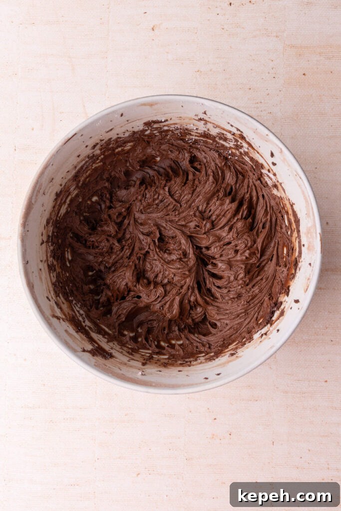 Thick chocolate fudge frosting freshly made in a large mixing bowl ready to pipe or spread.