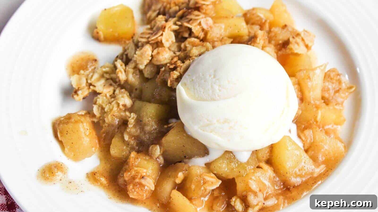A plate of apple crisp with chunks of apple, topped with a scoop of vanilla ice cream and an oat crumble topping.