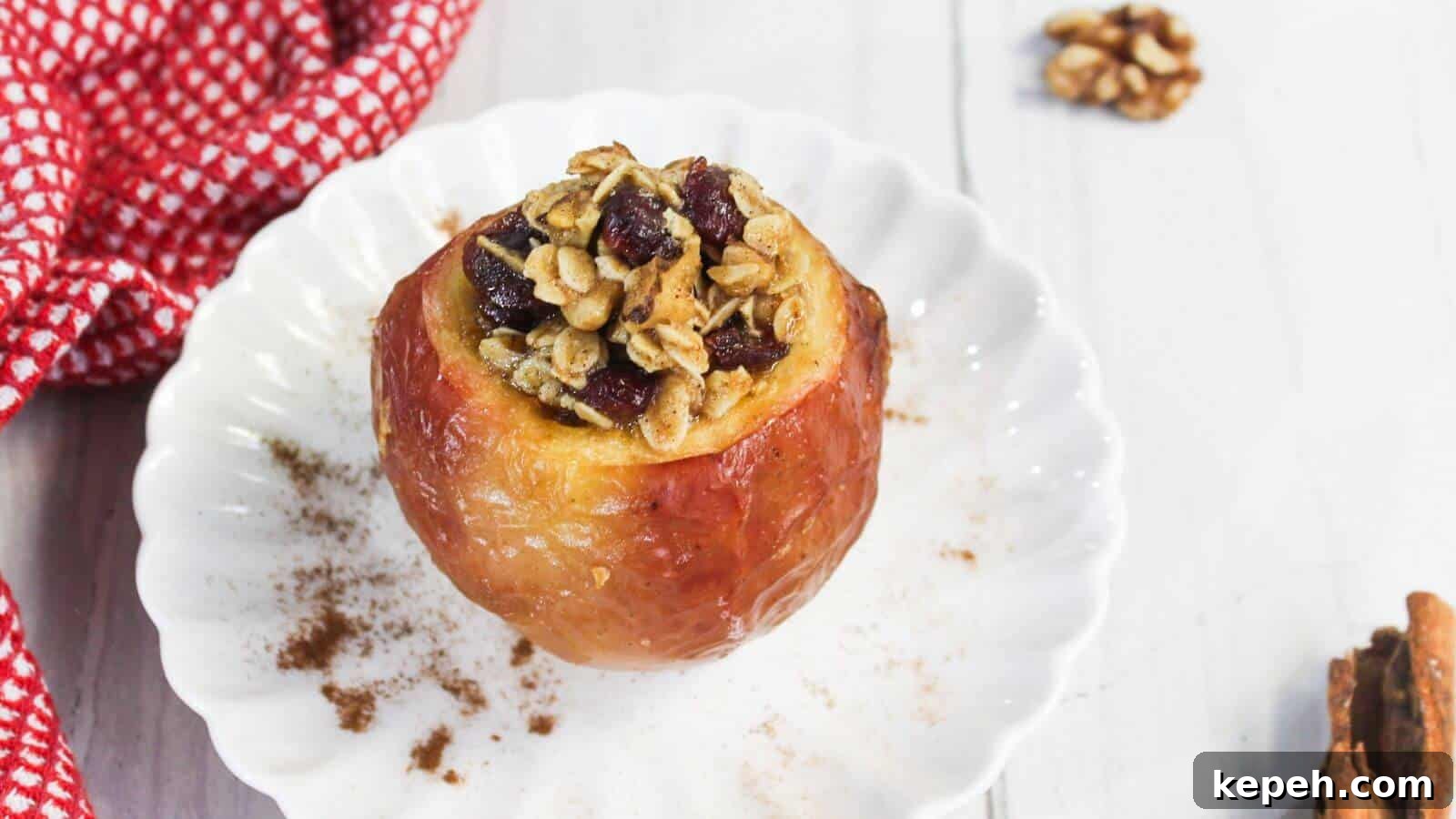 Baked apple on a white plate filled with oats, nuts, and cranberries, with cinnamon sprinkled around. A red checkered cloth is partially visible on the side.