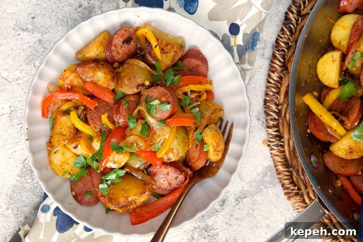 Smoked sausage and potatoes with red pepper and onions in a white bowl with a fork 