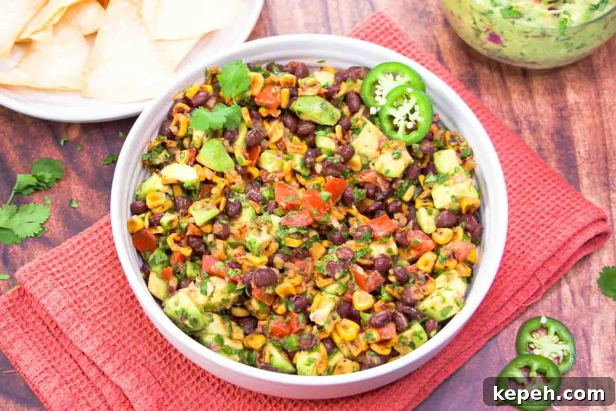 Fresh Avocado Salsa with Corn & Black Beans — Zesty Summer Dip 2 Angled view of a Avocado Salsa Dip served with tortilla chips for a summer appetizer. Hostess At Heart
