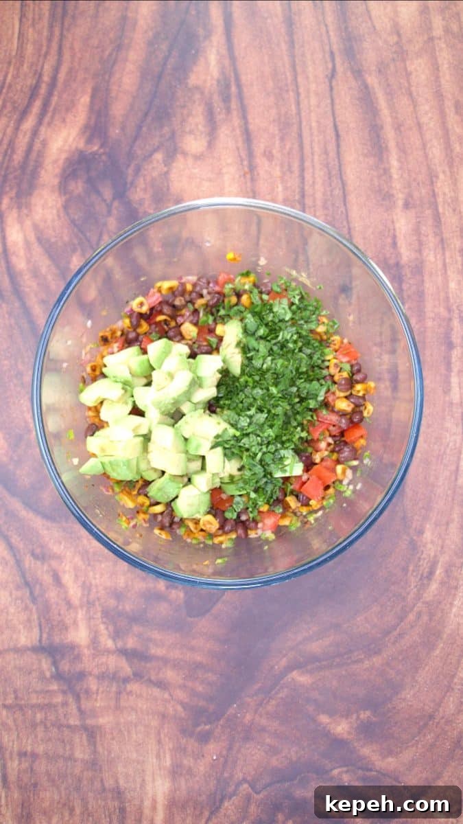 Fresh Avocado Salsa with Corn & Black Beans — Zesty Summer Dip 7 Fresh diced avocado and cilantro added to a mixing bowl filled with a black bean and corn salsa. Hostess At Heart