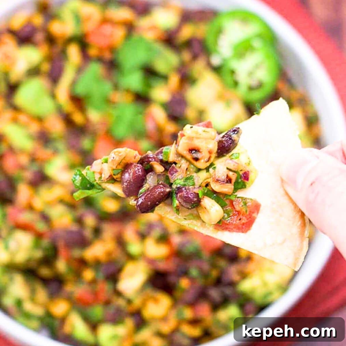 Fresh Avocado Salsa with Corn & Black Beans — Zesty Summer Dip 8 A tortilla chip filled with fresh avocado salsa as an appetizer. Hostess At Heart