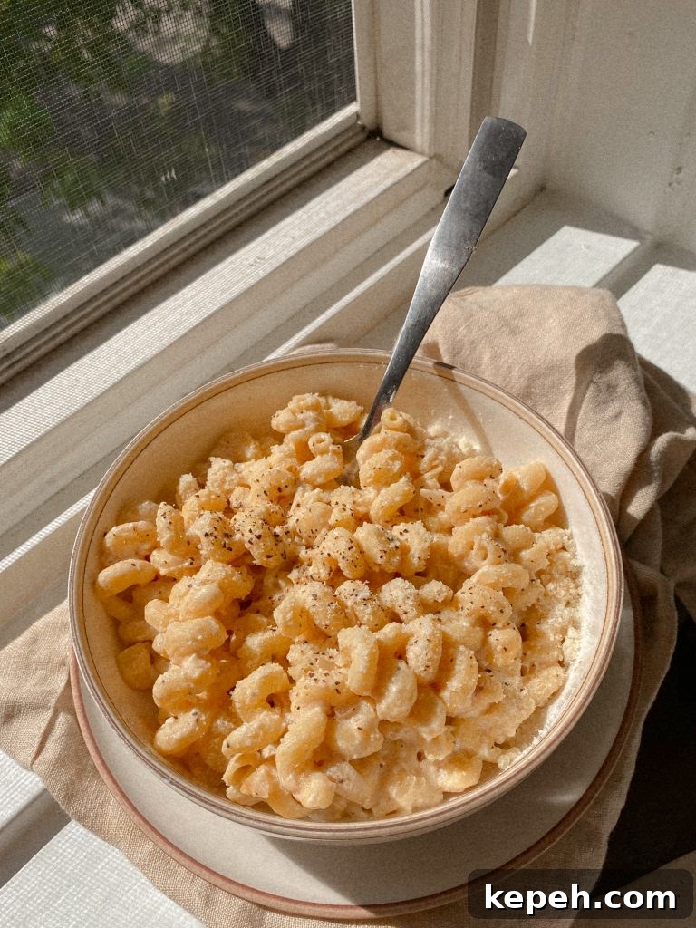 creamy cavatappi pasta in a white bowl with a dish towel on a window sill