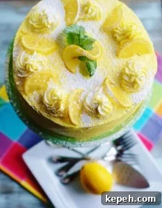 Triple Lemon Layer Cake iced with lemon yellow butter cream garnished with lemon slices, mint leaves, and powdered sugar.