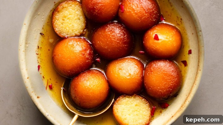 A bowl of Gulab Jamun with one cut in half showing the inside texture.