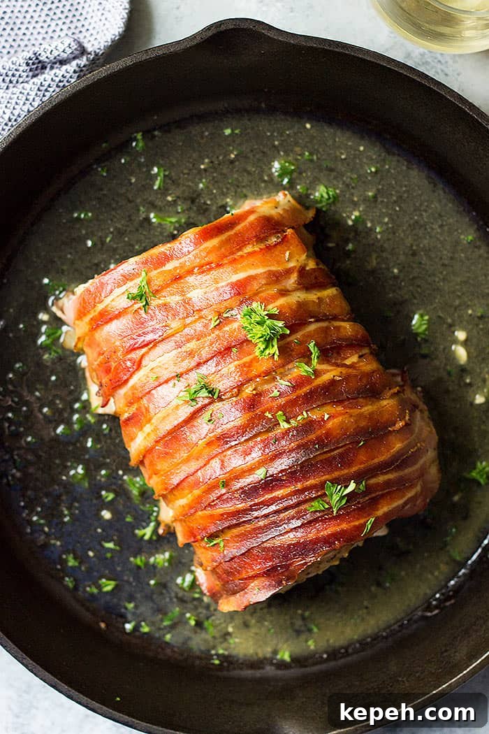 Pork loin wrapped in bacon in a cast iron skillet.
