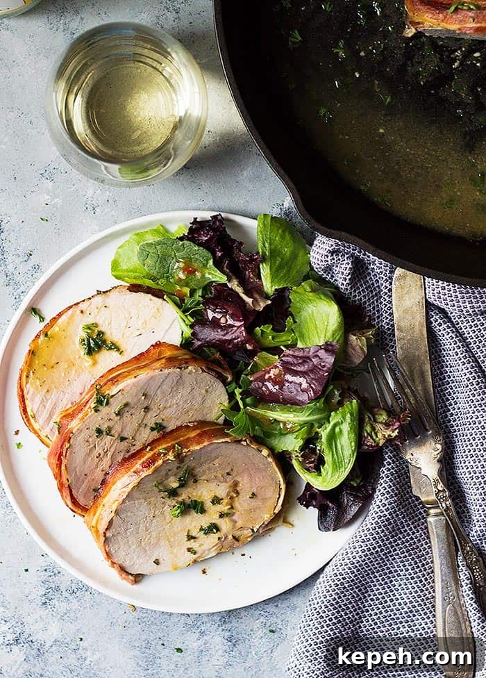 Sliced pork loin on plate with salad and utensils.