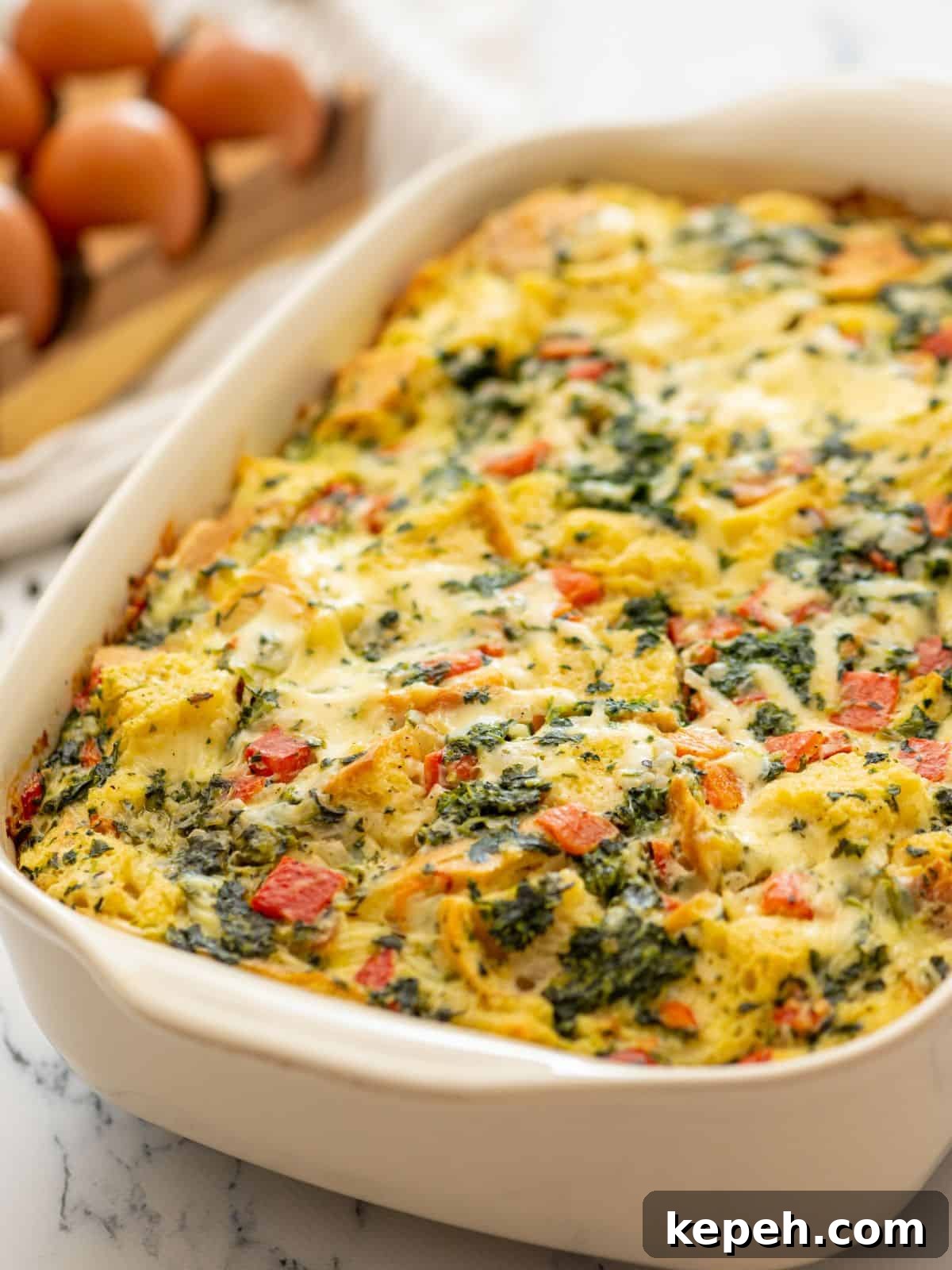 Baked breakfast strata with spinach and red peppers in baking dish.