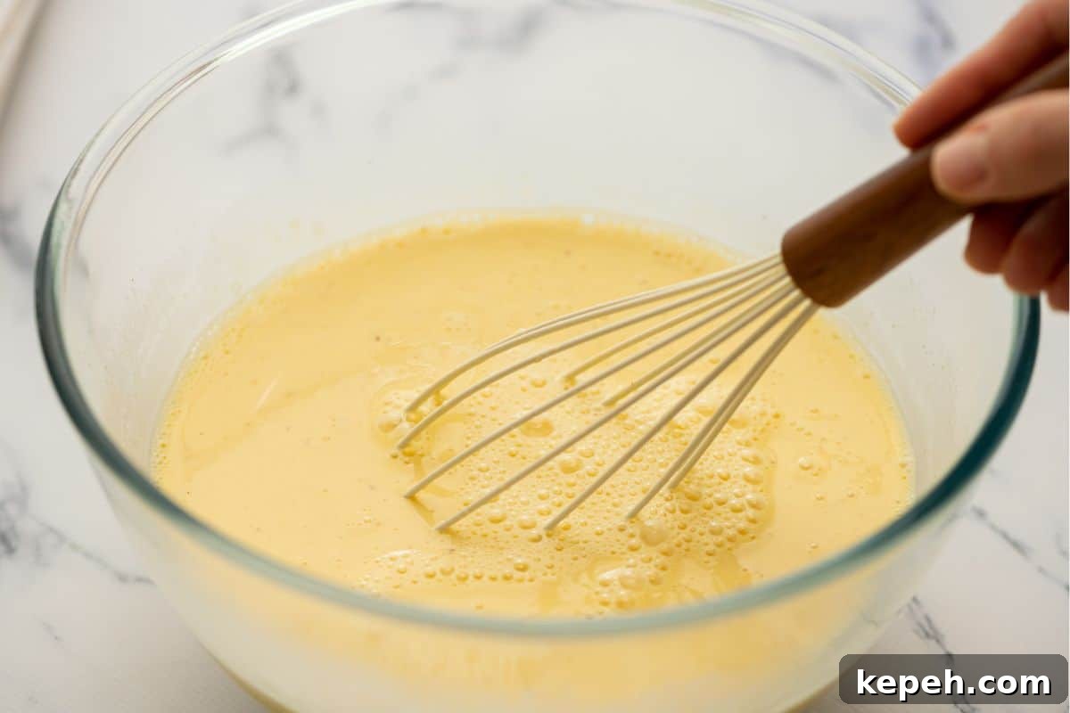 Whisk in bowl with eggs, cream, milk, and seasonings whisking together.