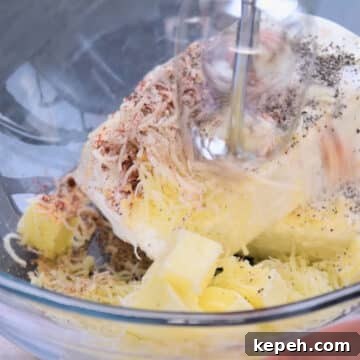 Cream cheese, butter, mozzarella cheese, salt, pepper, paprika, garlic powder in glass bowl being mixed with a hand held mixer. 