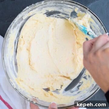 Cheese mixture being smoothed out with rubber spatula. 