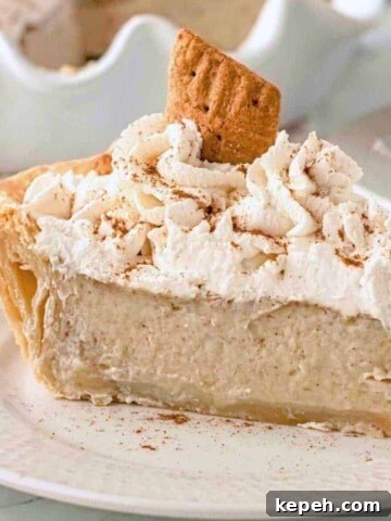 Single slice of baked banana pie with whipped cream and cinnamon on top, sitting on a white plate.